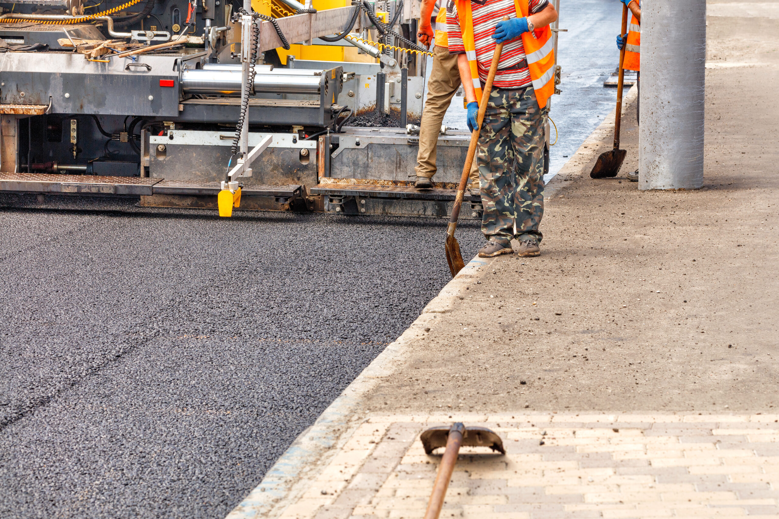 An industrial worker laying a layer of new hot asphalt on the carriageway